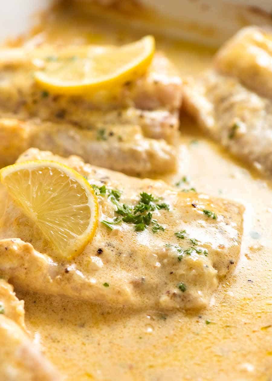 Close up photo of Baked Fish recipe with Lemon Cream Sauce in a white pan, fresh out of the oven