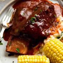 Beef Ribs in barbecue sauce on a plate with coleslaw and corn