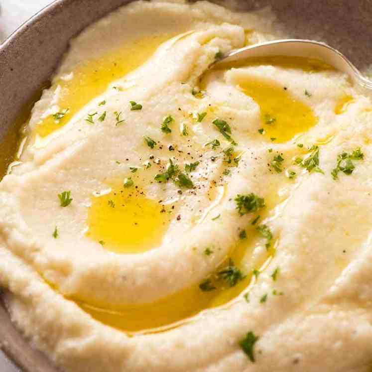 Rustic brown bowl of Creamy Cauliflower Mash topped with a drizzle of butter