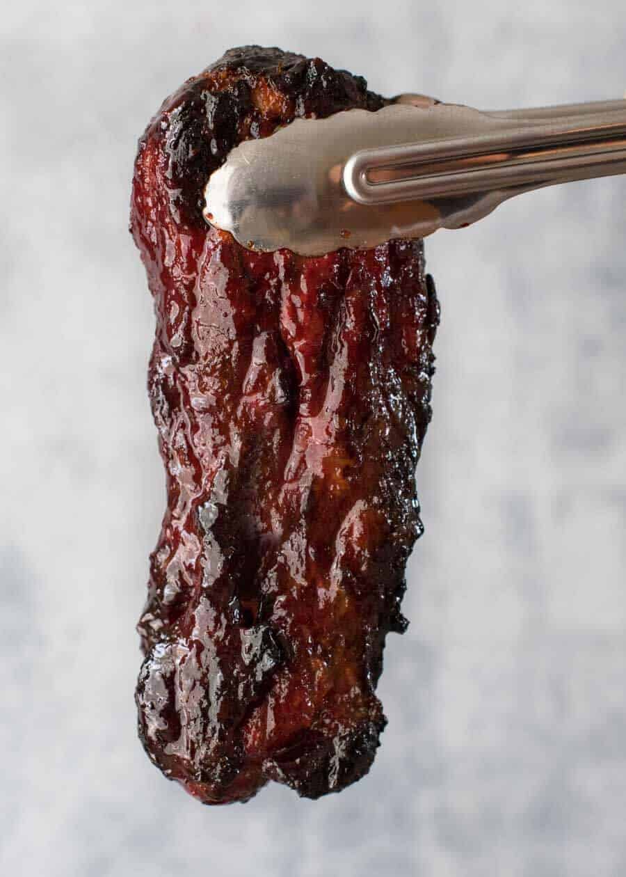 Char Siu (Chinese Barbecue Pork) being held by tongs, fresh out of the oven.