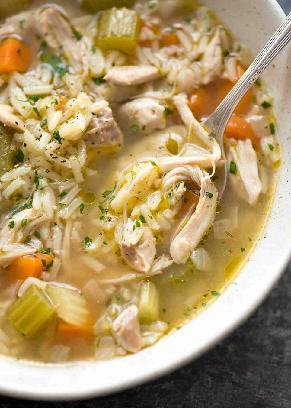 Close up of chicken and rice soup in a rustic beige bowl, ready to be eaten.