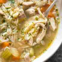 Close up of chicken and rice soup in a rustic beige bowl, ready to be eaten.