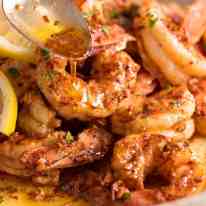 Close up of spoon drizzling Lemon Garlic Butter Sauce over grilled shrimp / prawns