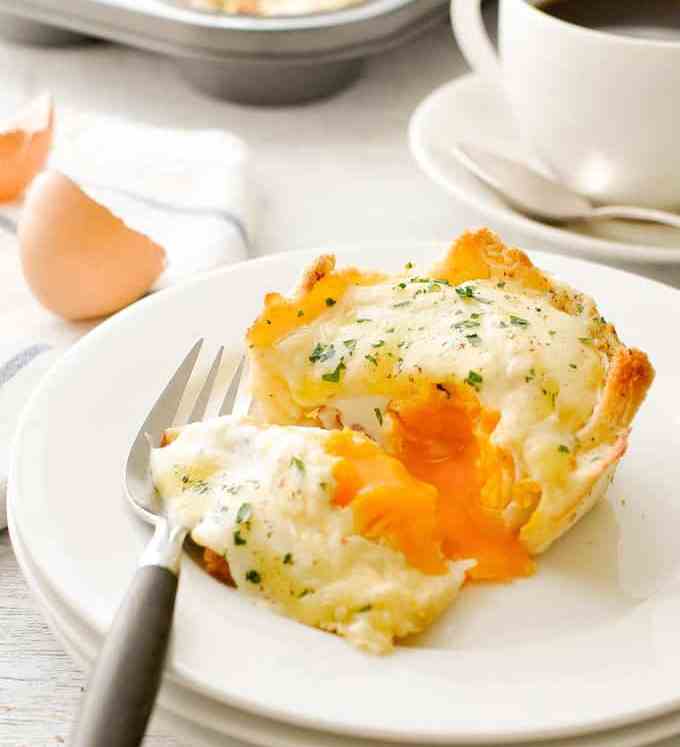 Muffin Tin Breakfast Croque Madame Toastie Cup on a white plate, cut open with runny egg yolk running out.