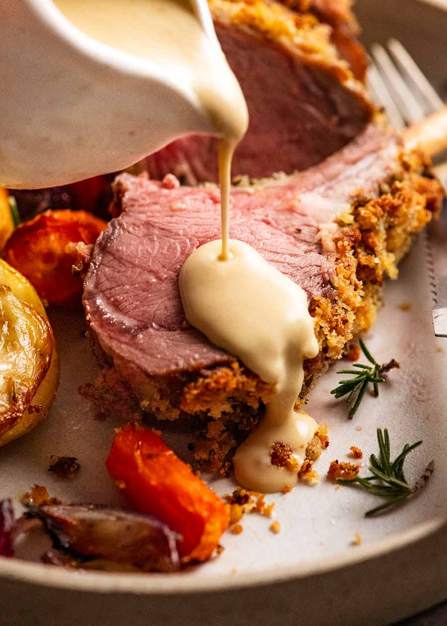 Pouring Creamy White Wine Mustard Sauce over Rosemary Crumbed Rack of Lamb