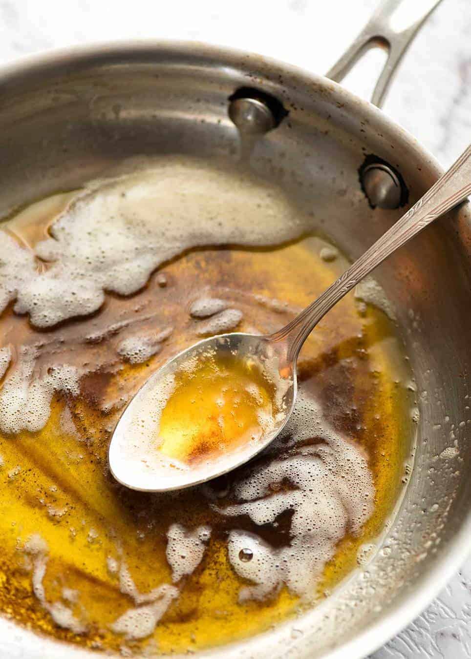 Brown butter in a small silver skillet with a spoon.