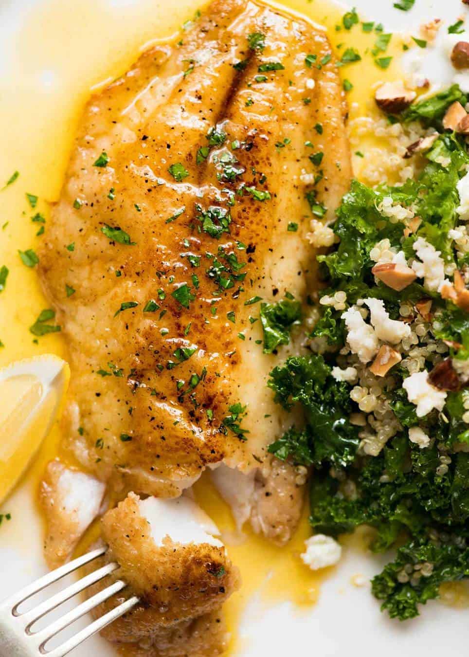 Overhead photo of a crispy pan fried fish fillet drizzled with Lemon Butter Sauce and sprinkled with parsley on a white plate with a side of Kale Quinoa Salad.