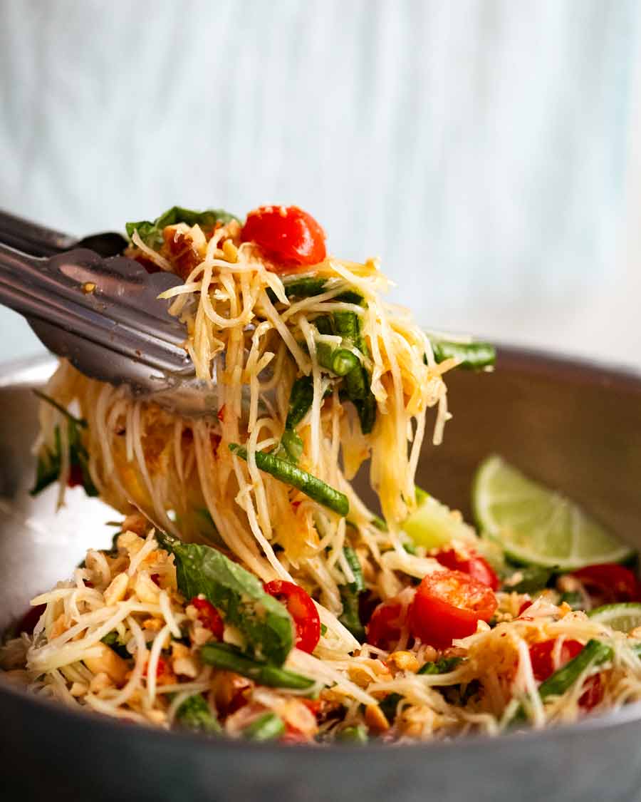 Tongs picking up freshly made Green Papaya Salad (Thai)