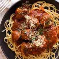 Overhead photo of Italian Meatballs in a rustic black bowl garnished with parmesan, ready to be eaten