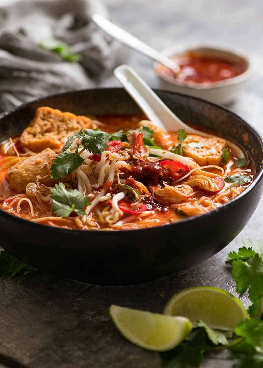 Laksa soup in a black bowl with toppings and Laksa chilli sauce, ready to be eaten