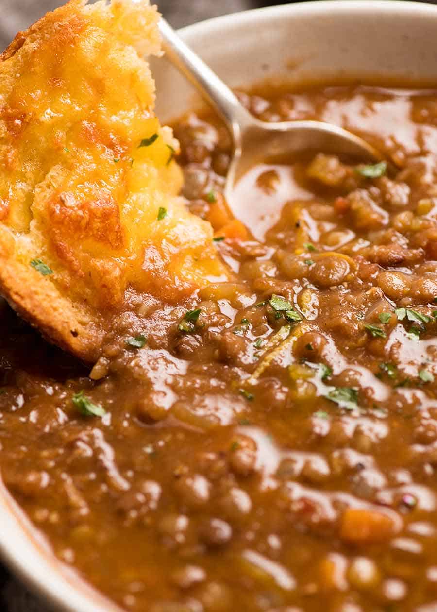 Close up of cheesy garlic bread being dunked into Lentil Soup