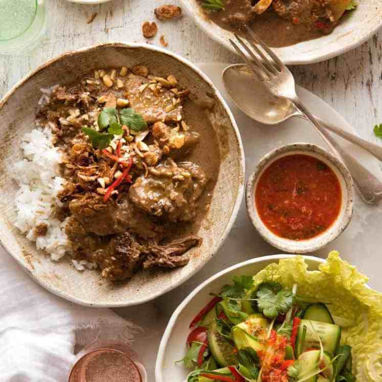 Overhead photo of two bowls with Massaman Curry on rice with a side salad, ready to be eaten