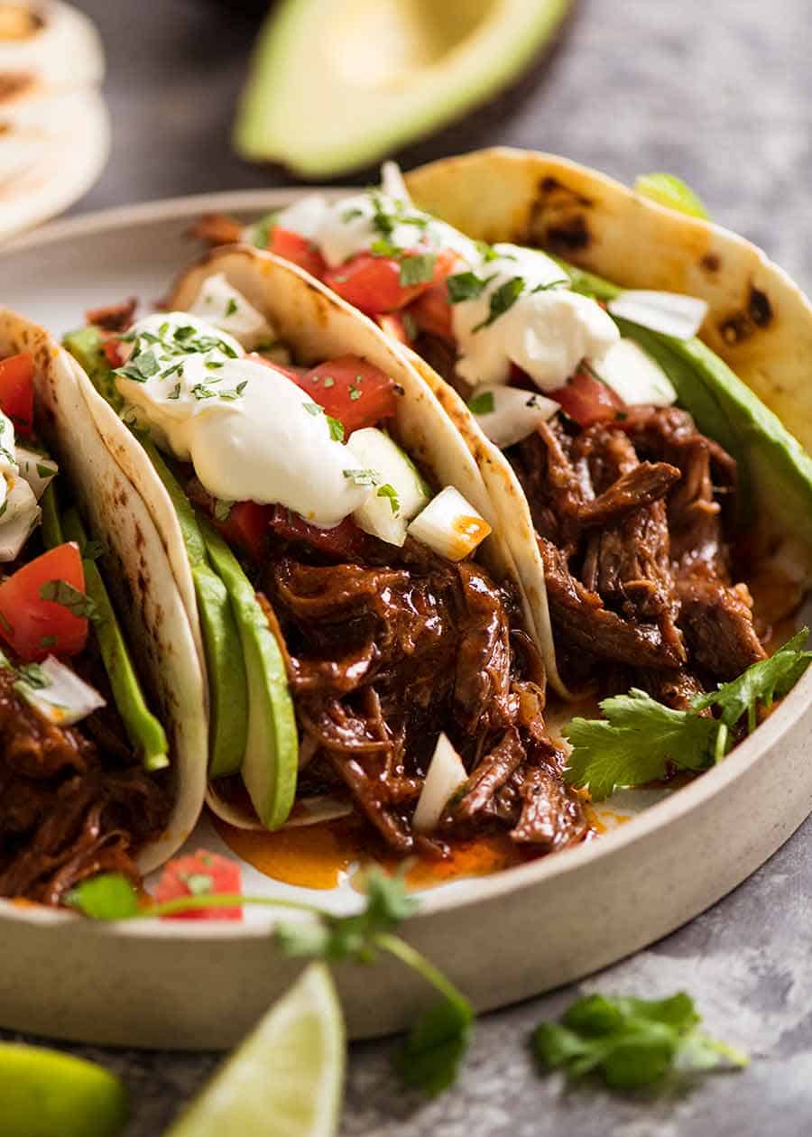 Close up of 3 Mexican Shredded Beef Tacos on a plate with pico de Gallo, avocado, and sour cream