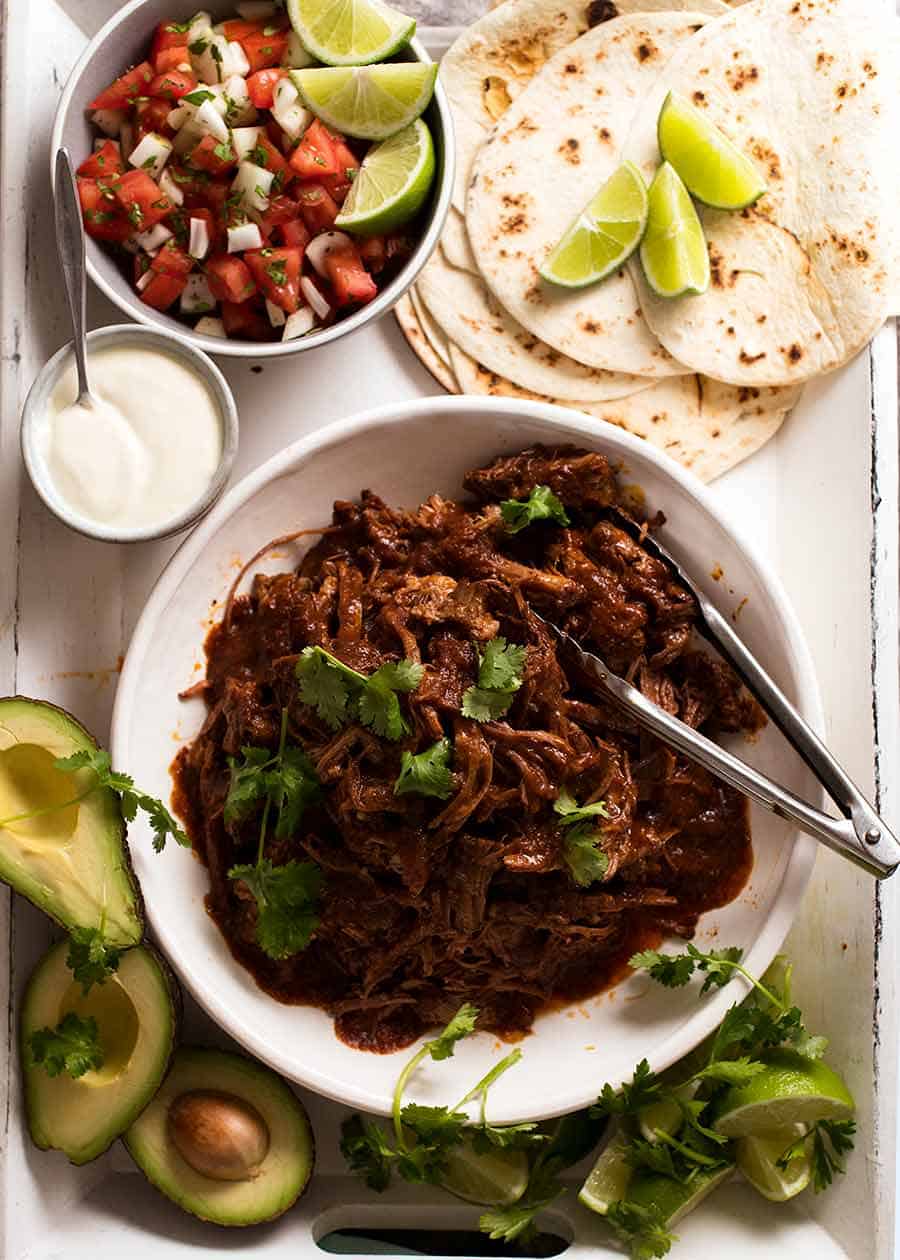 Overhead photo of Mexican Shredded Beef taco spread - tortillas, sour cream, avocado, lime, pico de Gallo