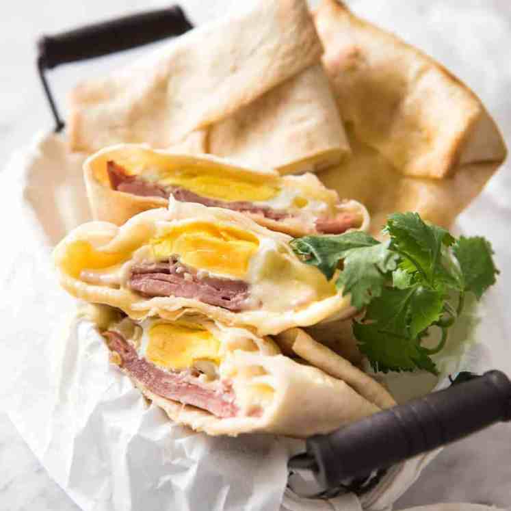 Hot Ham, Egg and Cheese Pockets made with tortillas in a basket, with some cut showing the inside with molten cheese and perfectly cooked egg.