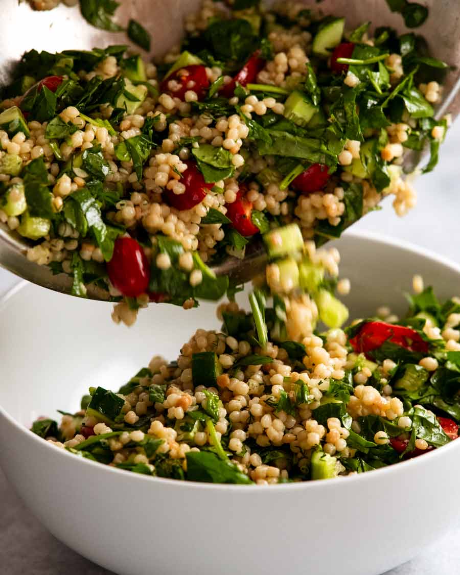 Pouring Pearl couscous salad into a serving bowl