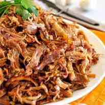 Pile of golden, crispy and juicy Pork Carnitas on a white plate.