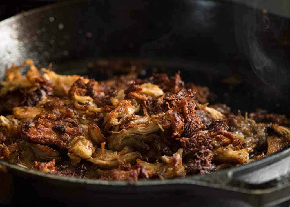 Pork Carnitas being crisped to golden in a black skillet.