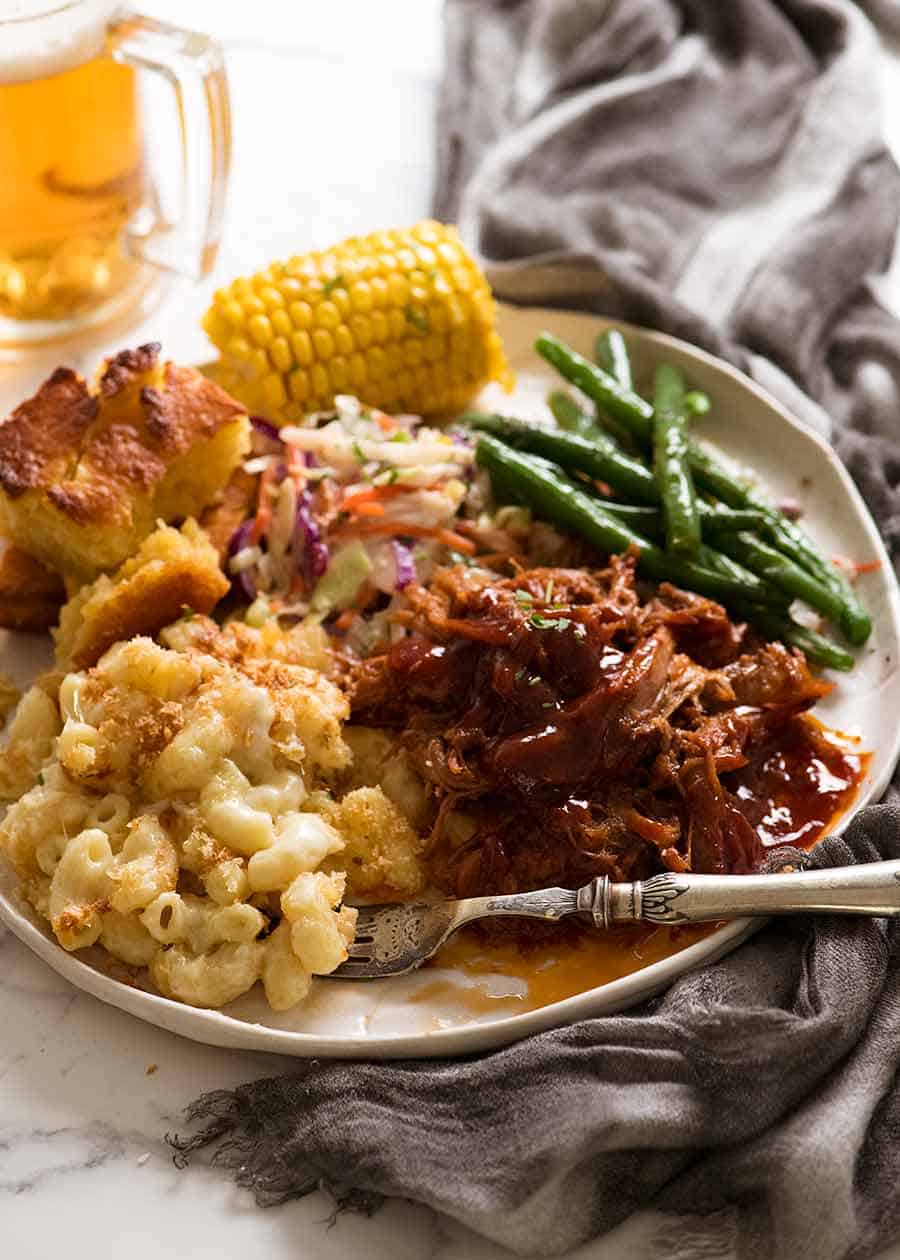 Dinner plate with Pulled pork with BBQ Sauce with side dishes - Mac and Cheese, steamed greens, cornbread and steamed corn