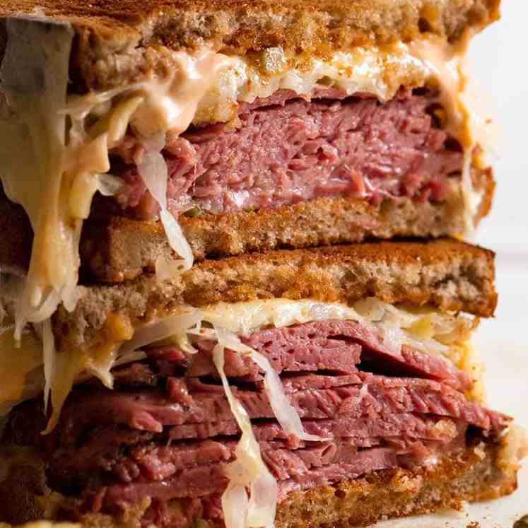 Reuben Sandwich loaded with homemade pastrami, easy quick sauerkraut, Russian Dressing, Swiss cheese on rye bread, ready to be eaten. Katz's deli copycat recipe.