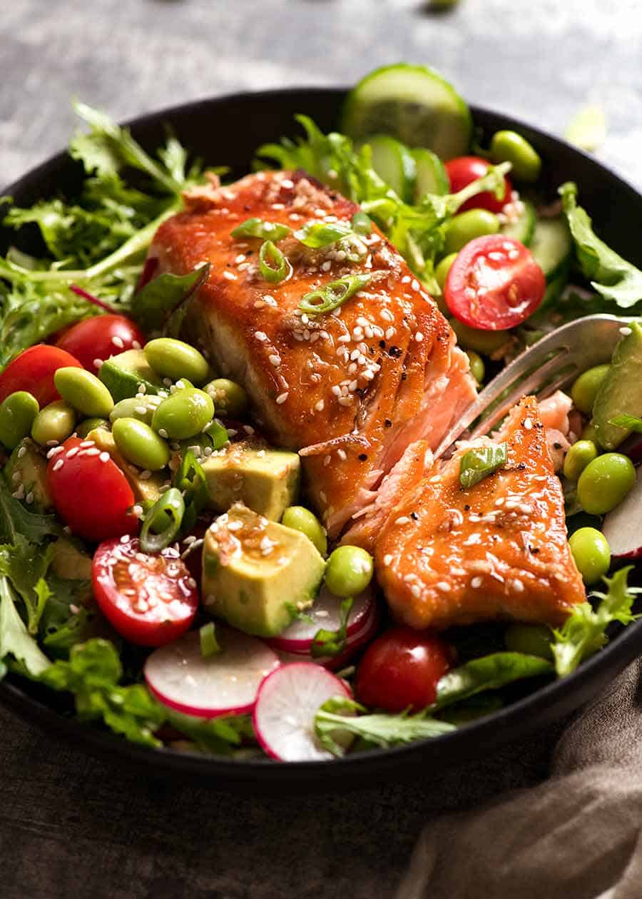 Close up of Asian Salmon Salad on a plate with edamame, avocado, tomato, radish and lettuce, with Asian Sesame Dressing