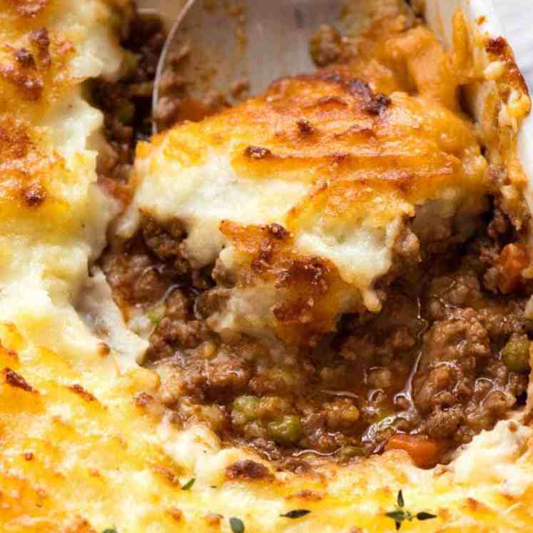 Close up of spoon scooping Shepherd's Pie out of a white baking dish, fresh out of the oven