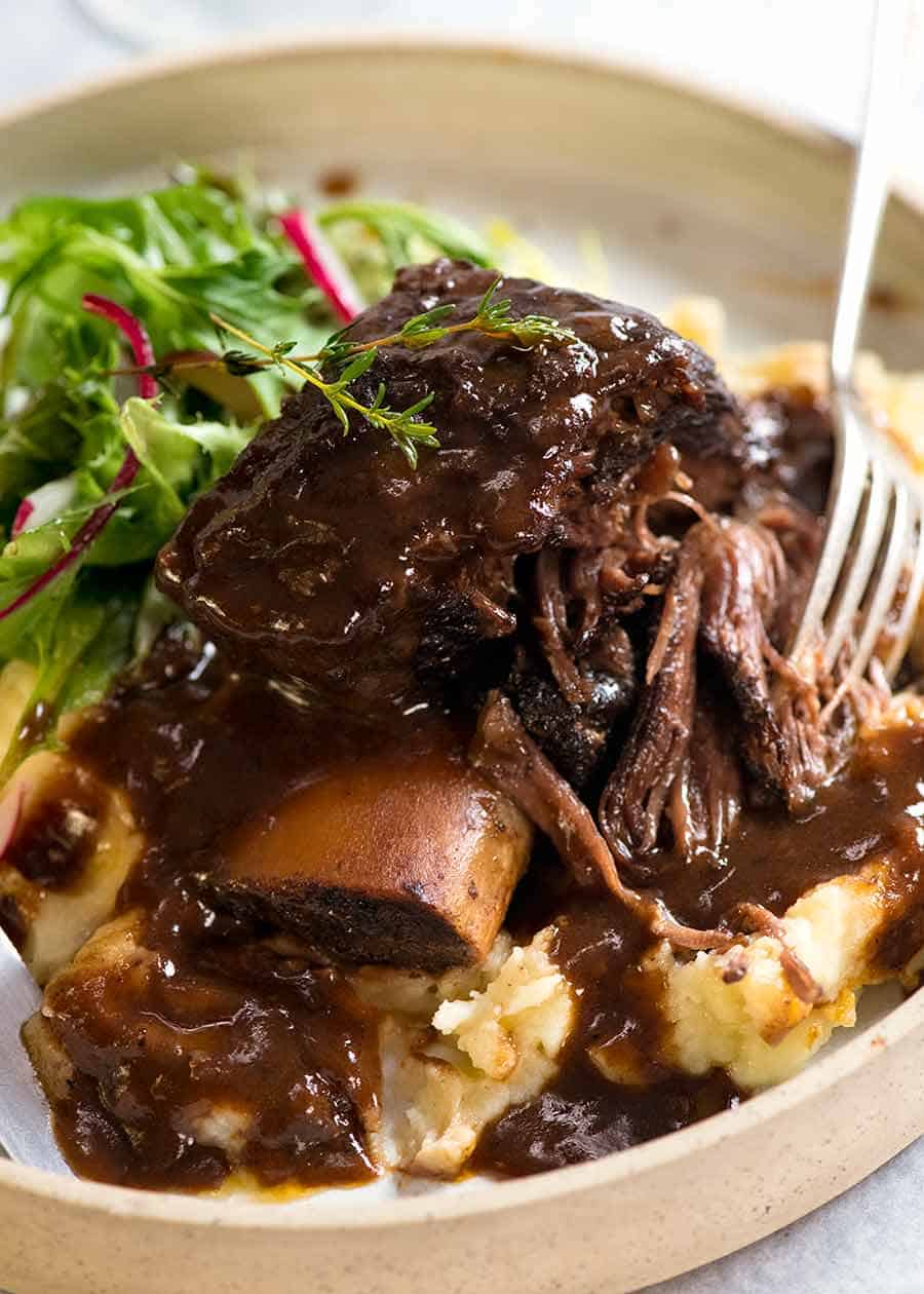 Close up of Slow Braised Beef Short Ribs in Red Wine Sauce on mashed potato on a rustic white plate, ready to be eaten