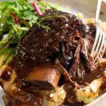 Close up of Slow Braised Beef Short Ribs in Red Wine Sauce on mashed potato on a rustic white plate, ready to be eaten