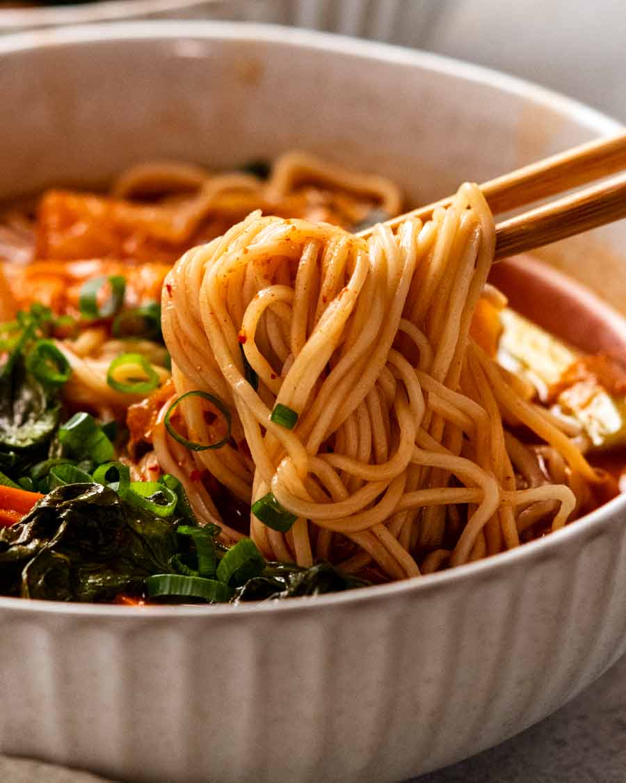 Chopsticks picking up noodles in Spicy Korean noodle soup