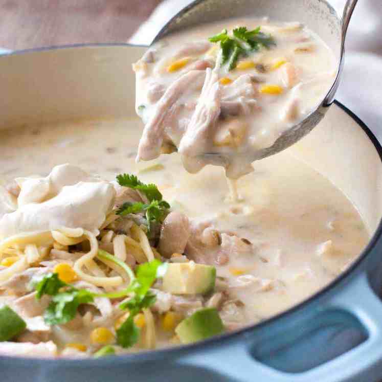 White Chicken Enchilada Soup being ladled out of a pale blue casserole pot.